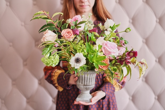 Young female florist holding  bouquet of pastel carnations and eucalyptus against a pink wall.