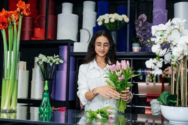 A young female florist takes care of flowers in a cozy flower shop and collects bouquets Floristry and making of buckets in a flower shop Small business