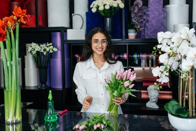 A young female florist takes care of flowers in a cozy flower shop and collects bouquets Floristry and making of buckets in a flower shop Small business