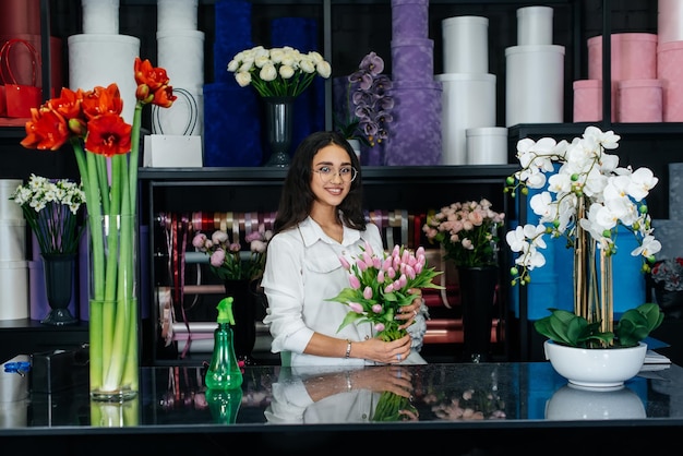 A young female florist takes care of flowers in a cozy flower shop and collects bouquets Floristry and making of buckets in a flower shop Small business