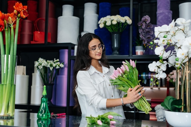 A young female florist takes care of flowers in a cozy flower shop and collects bouquets Floristry and making of buckets in a flower shop Small business