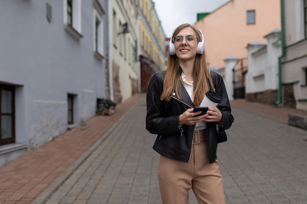 Young female freelancer music lover wearing headphones and walking in the city street