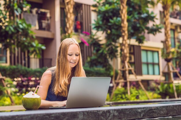 Young female freelancer sitting near the pool with her laptop in the hotel browsing in her