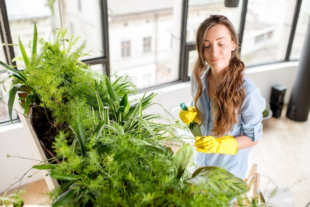 Young female gardener taking care of plants standing with watering can on the ladder in the orangery