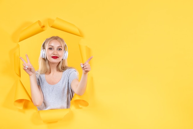 Young female in headphones pointing at something on yellow background audio sound ultrasound