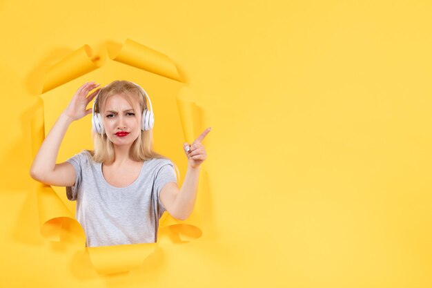 Young female in headphones pointing at something on yellow wall