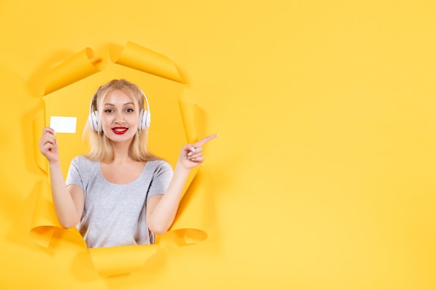 Young female in headphones with credit card on yellow background audio ultrasound music