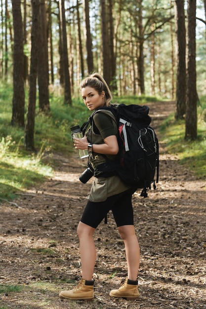 Young female hiker with big backpack and reusable bottle for water in green forest