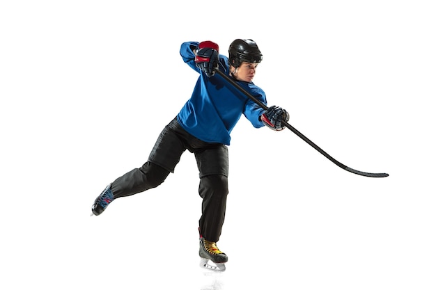 Young female hockey player with the stick on ice court and white wall. Sportswoman wearing equipment and helmet training. Concept of sport, healthy lifestyle, motion, action, human emotions.