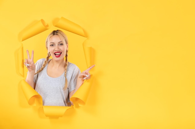 Young female looking from torn yellow paper background emotion indoor sale window