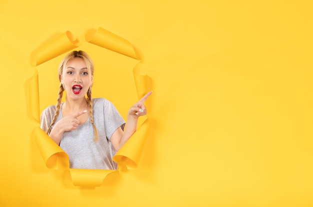 Young female looking from torn yellow paper background window indoor sale