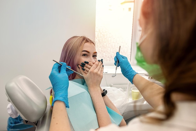 Young female patient sits dentist closes her mouth from female dentist because she is afraid