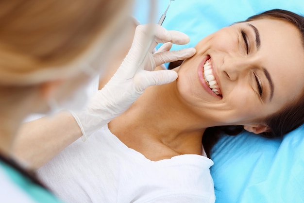 Young female patient visiting dentist office.Beautiful woman with healthy straight white teeth sitting at dental chair with open mouth during oral checkup while doctor working at teeth. Dental clinic,