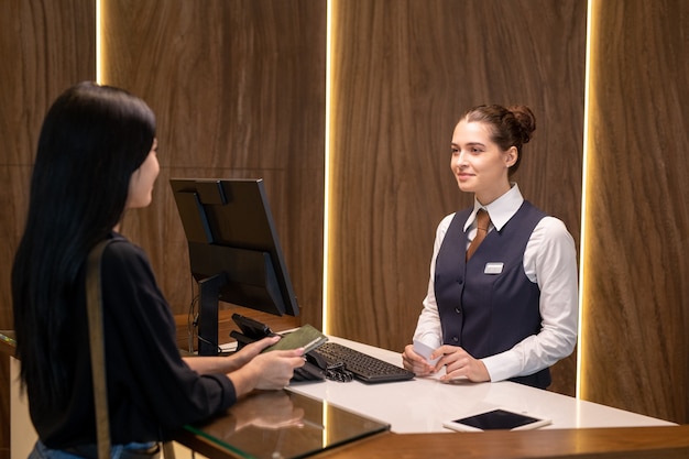 Young female receptionist serving one of clients by counter