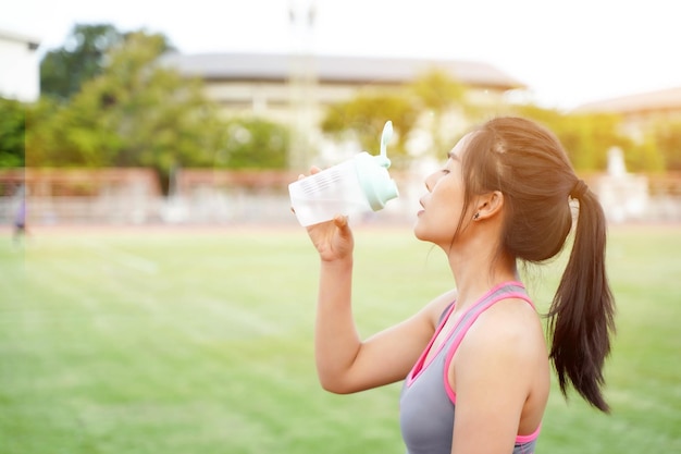 Young female relaxing and drinking water after fitness training at the football stadium in the morning