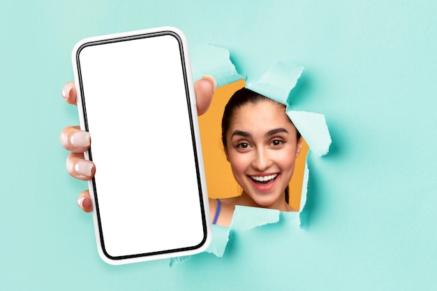 Young female showing black empty smartphone screen through torn paper