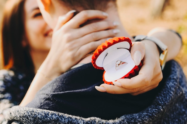 Photo young female smiling and hugging anonymous male while holding box with elegant engagement ring and standing in nature on sunny day