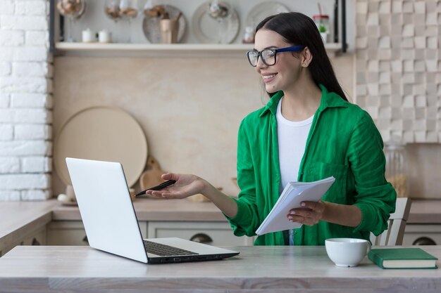 A young female student a freelancer studies works online at home from a laptop he sits at the table