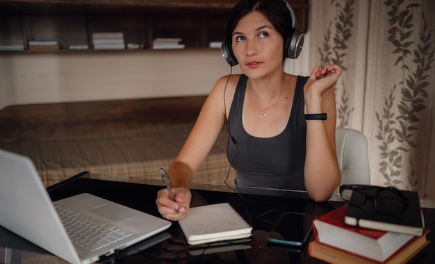 Young female student in headphones using laptop communicates on internet with teachers