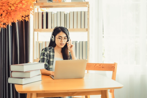 Young female student in plaid shirt sitting at the table using laptop when studying.