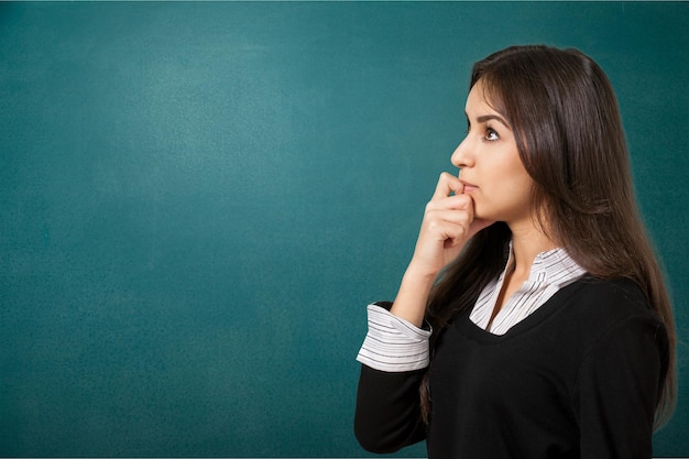 A young female student standing in front of the blackboard and looking at something.