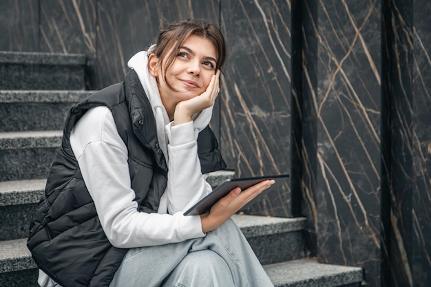 A young female student stands with a digital tablet in her hands outside