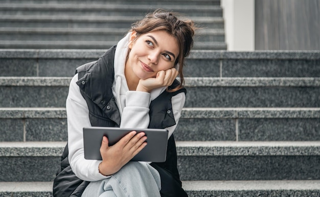 A young female student stands with a digital tablet in her hands outside