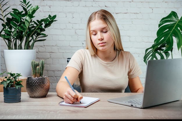 Young female student studying online and making notes