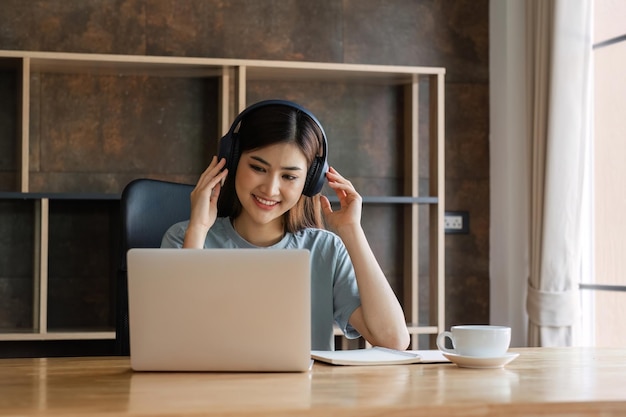 Young female student wearing headphones sits intently and happily studying online on her laptop in the living room at home