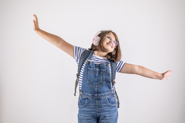 Young female student with backpack has headphones on and arms wide apart dreaming looking up