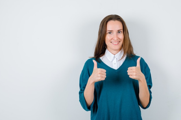 Photo young female in sweater over shirt showing double thumbs up and looking cheerful , front view.