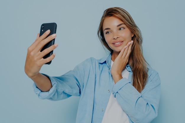 Young female taking photo isolated on light blue background