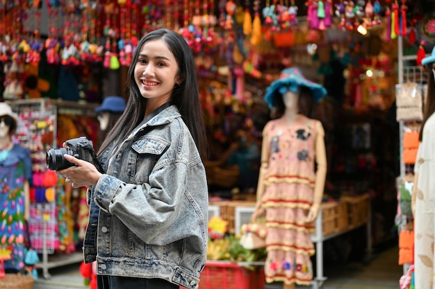 Young female tourist smiling to the camera and holding camera in the local market