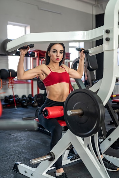 Young female training trains the muscles of the arms and press on the simulator in gym