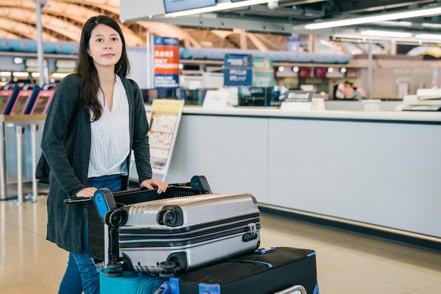 young female traveler pushing cart leaving walking to the gate after checked in. busy counter in the kix airport. attractive tourist finished travel in japan lifestyle concept.