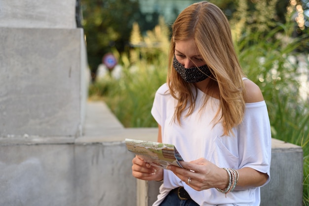 A young female trying to find a place with the help of a map on a street with a face mask