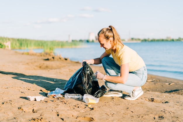 Young female volunteer satisfied with picking up trash a plastic bottles and coffee cups clean up