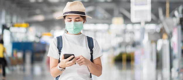 Young female wearing face mask and using mobile smartphone in airport terminal