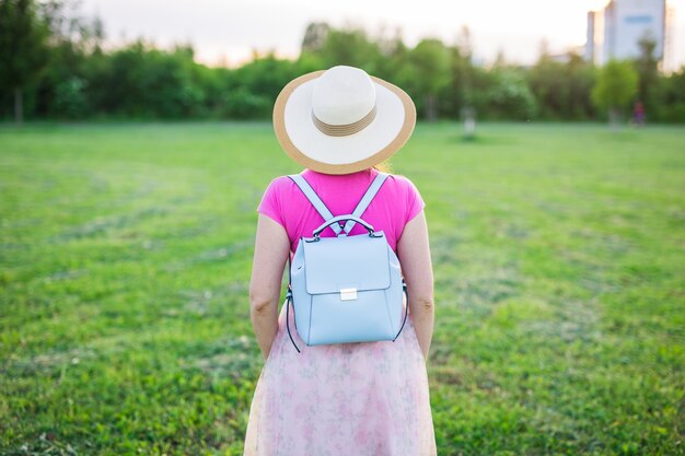 Young female with blue backpack and hat enjoying the countryside back view