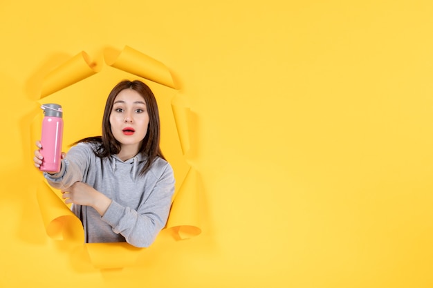 young female with bottle of water on torn yellow paper background indoor gym fit