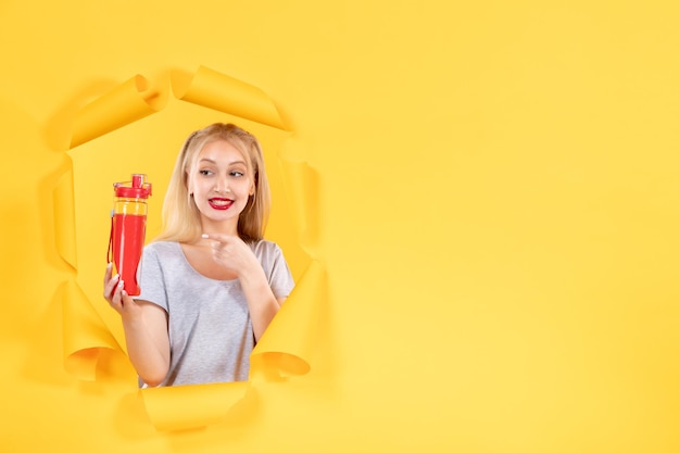 Young female with red bottle on a yellow wall