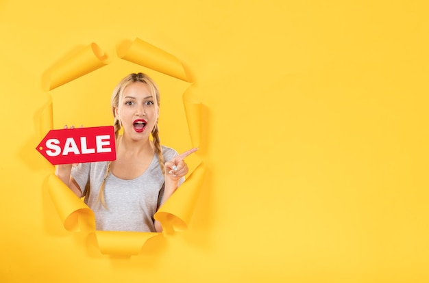 Young female with sale inscription sign on torn yellow paper background indoor shopping facial