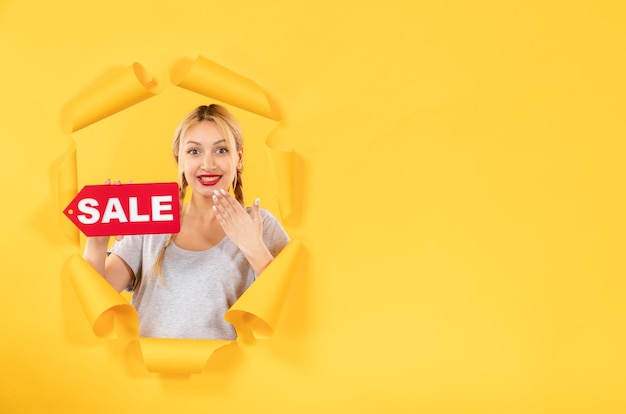 Young female with sale inscription sign on torn yellow paper surface shopping indoor facial