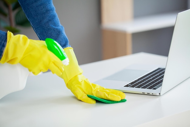 Young female worker cleaning office in yellow gloves