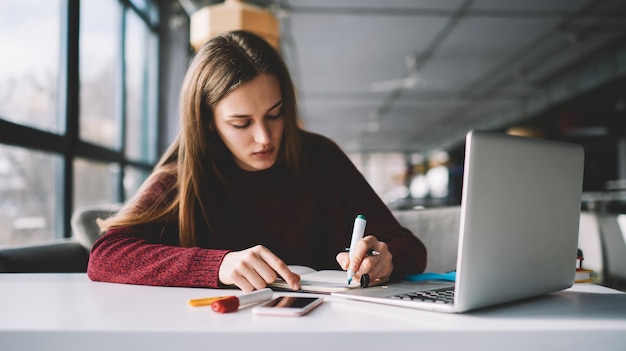 Young female writer scribing notes to textbook prepare for exam girl doing homework sitting desktop