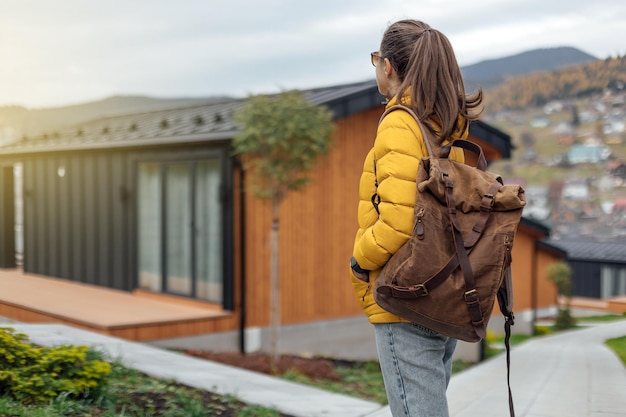 Young female in yellow down jacket with leather retro tourism backpack have a walk in nature backgro