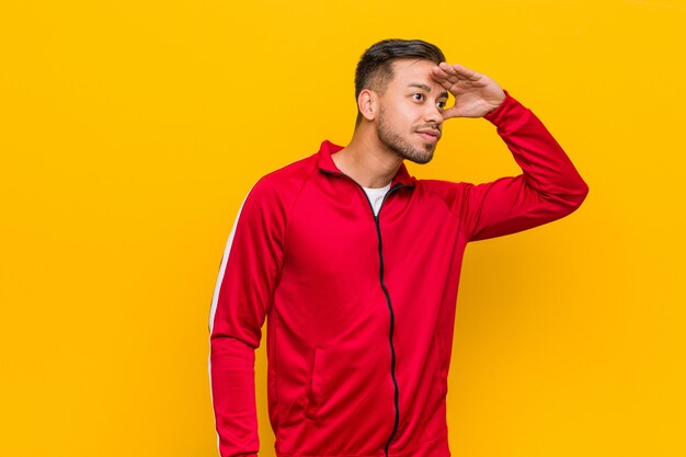 Photo young filipino fitness man looking far away keeping hand on forehead.