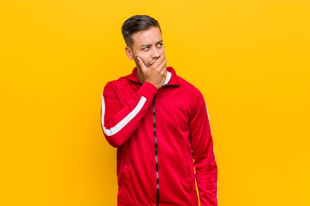 Young filipino fitness man thoughtful looking to a copy space covering mouth with hand.