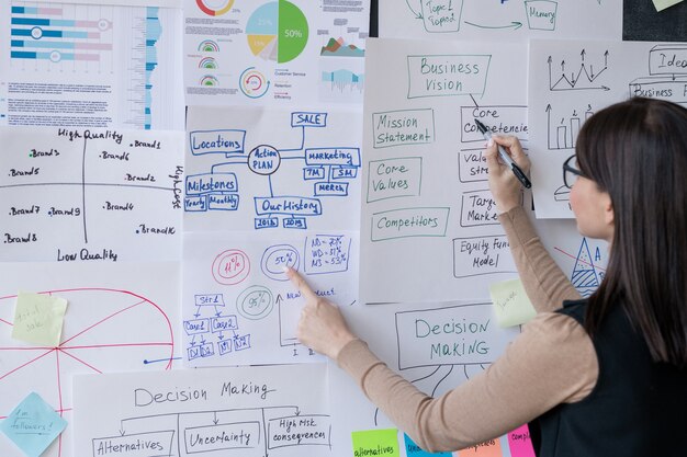 Young financial analyst pointing at papers with charts on blackboard while presenting analysis of data at seminar