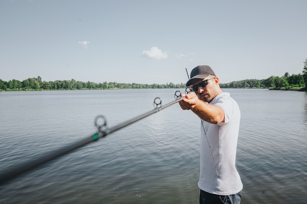 Young fisherman fishing on lake or river. Concentrated serious guy holding long rod with hands and looking forward. Geting ready for fishing.